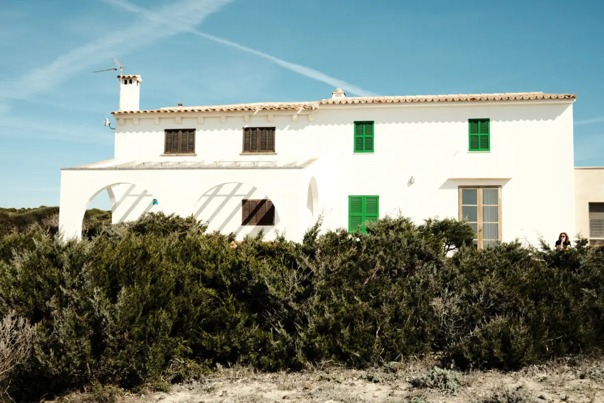 Weiße Finca mit grünen Fensterläden hinter Büschen