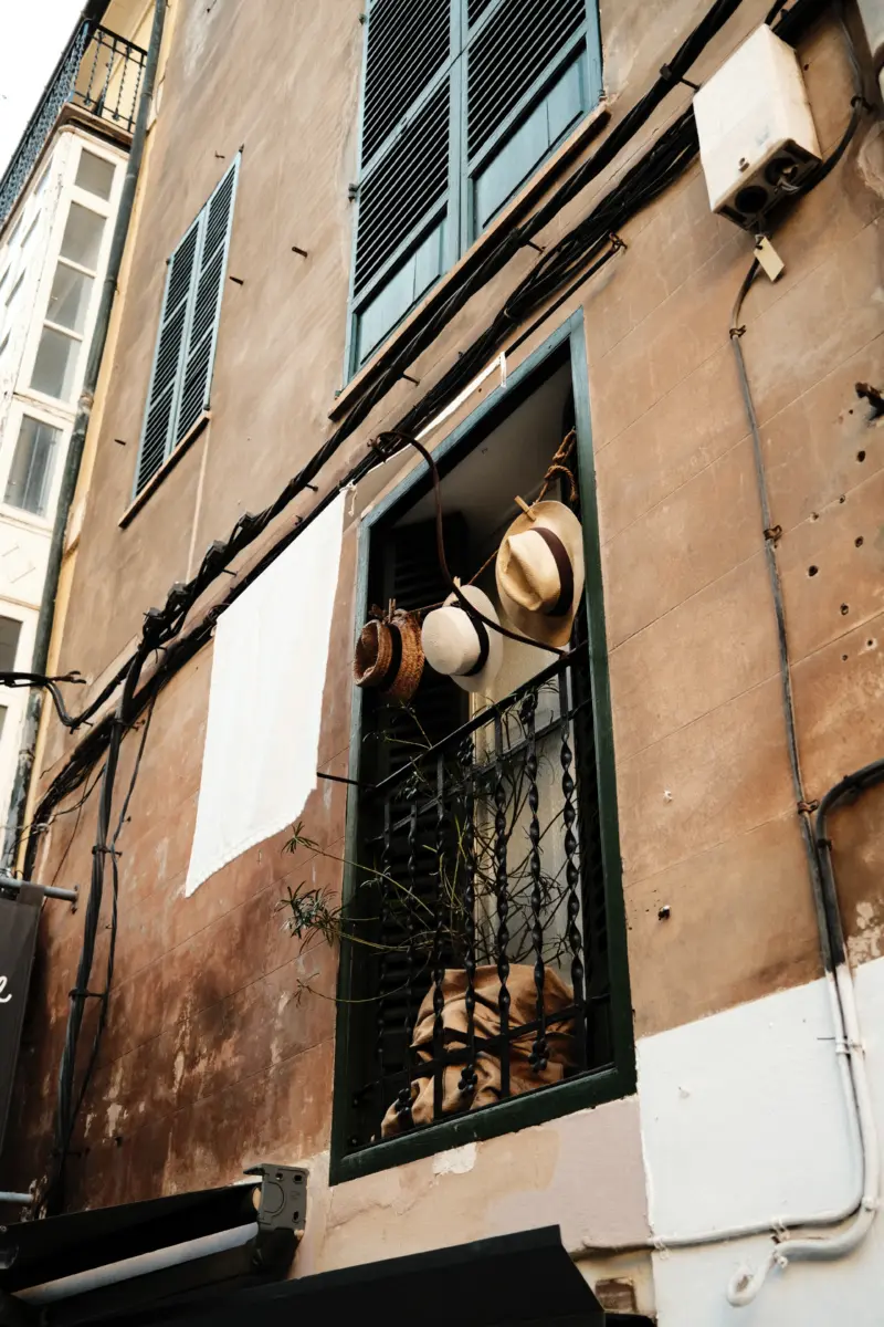 Alte Fassade mit Fensterläden und Hüten im offenen Fenster