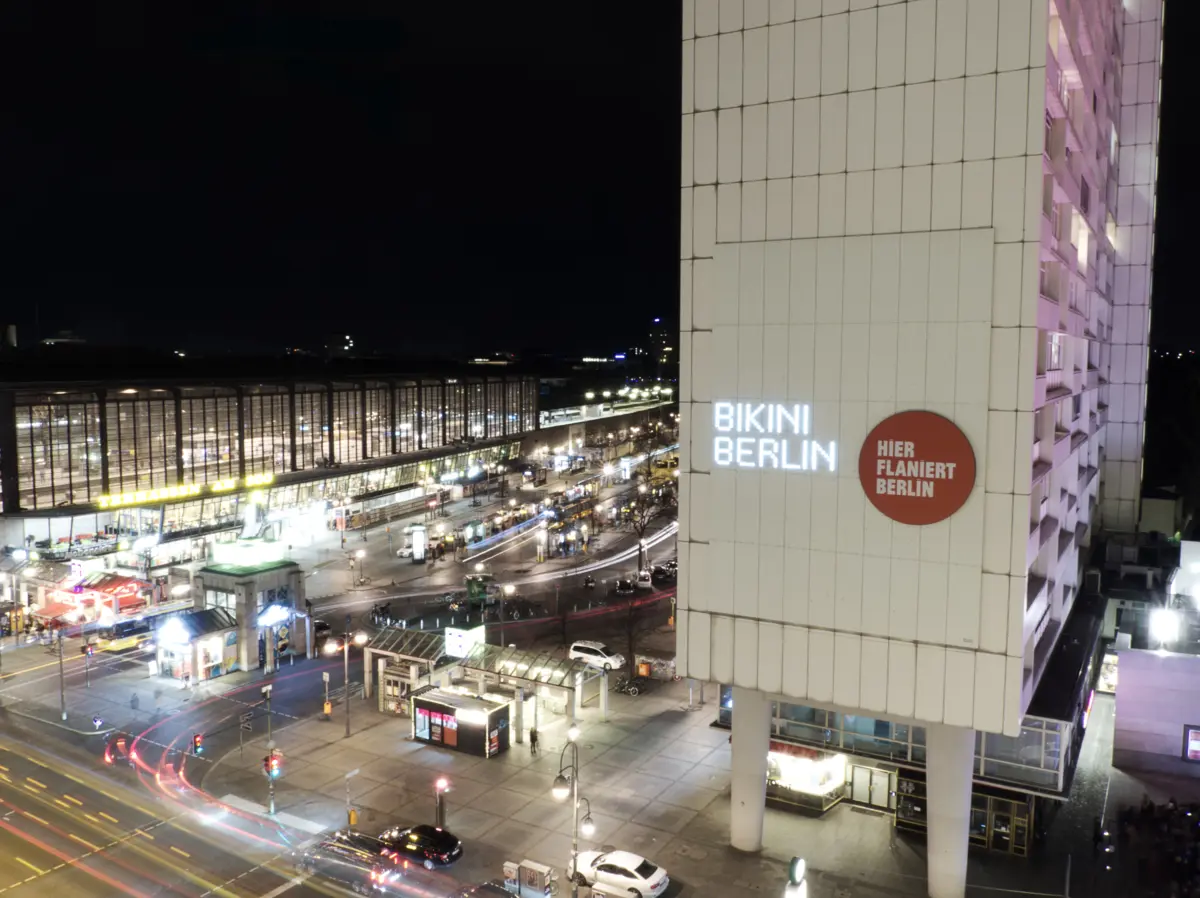 Bahnhofsplatz bei Nacht mit Leuchtschrift „Bikini Berlin“