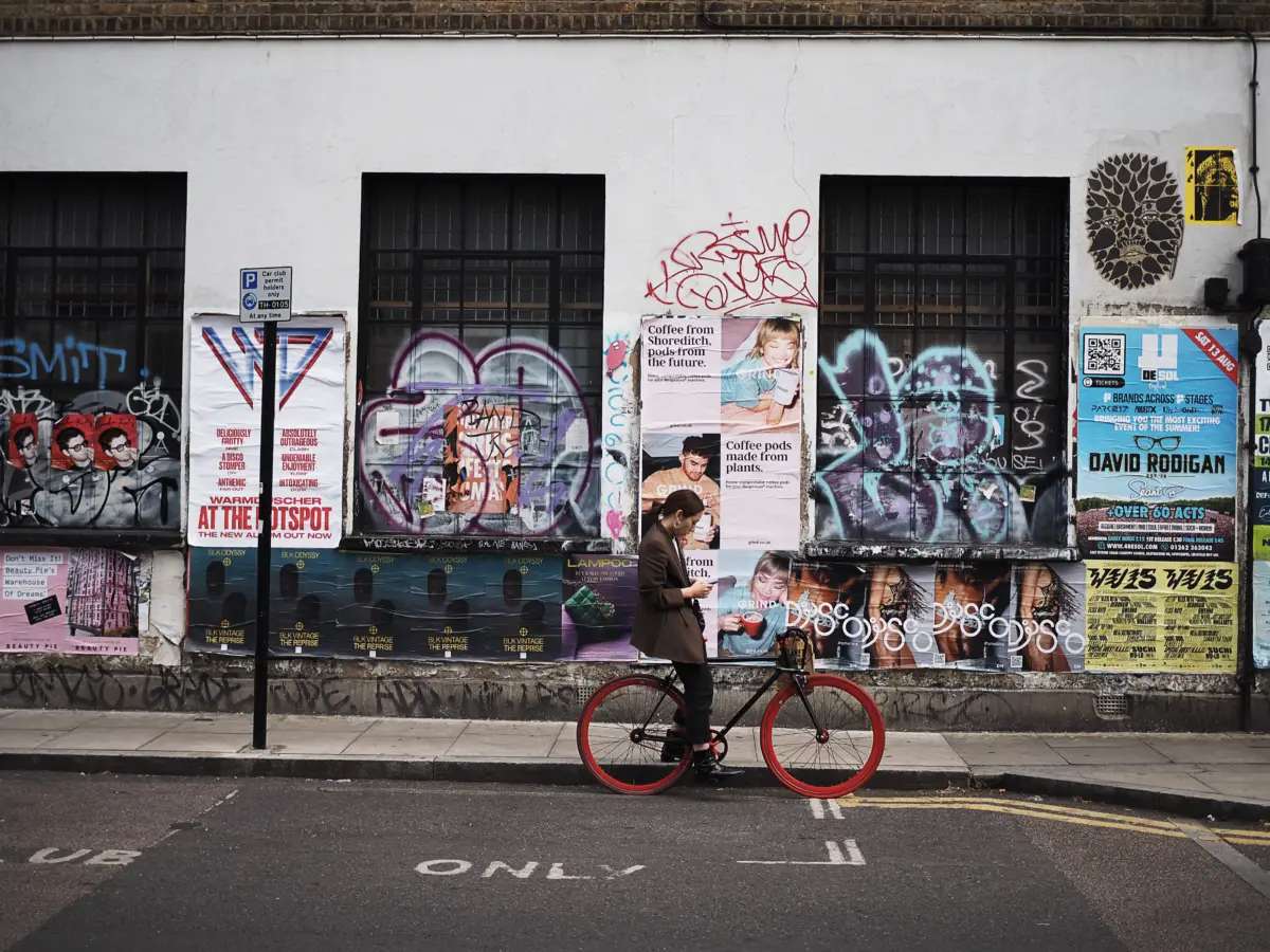 Radfahrer mit rotem Fahrrad vor einer Wand voller Graffiti und Plakate