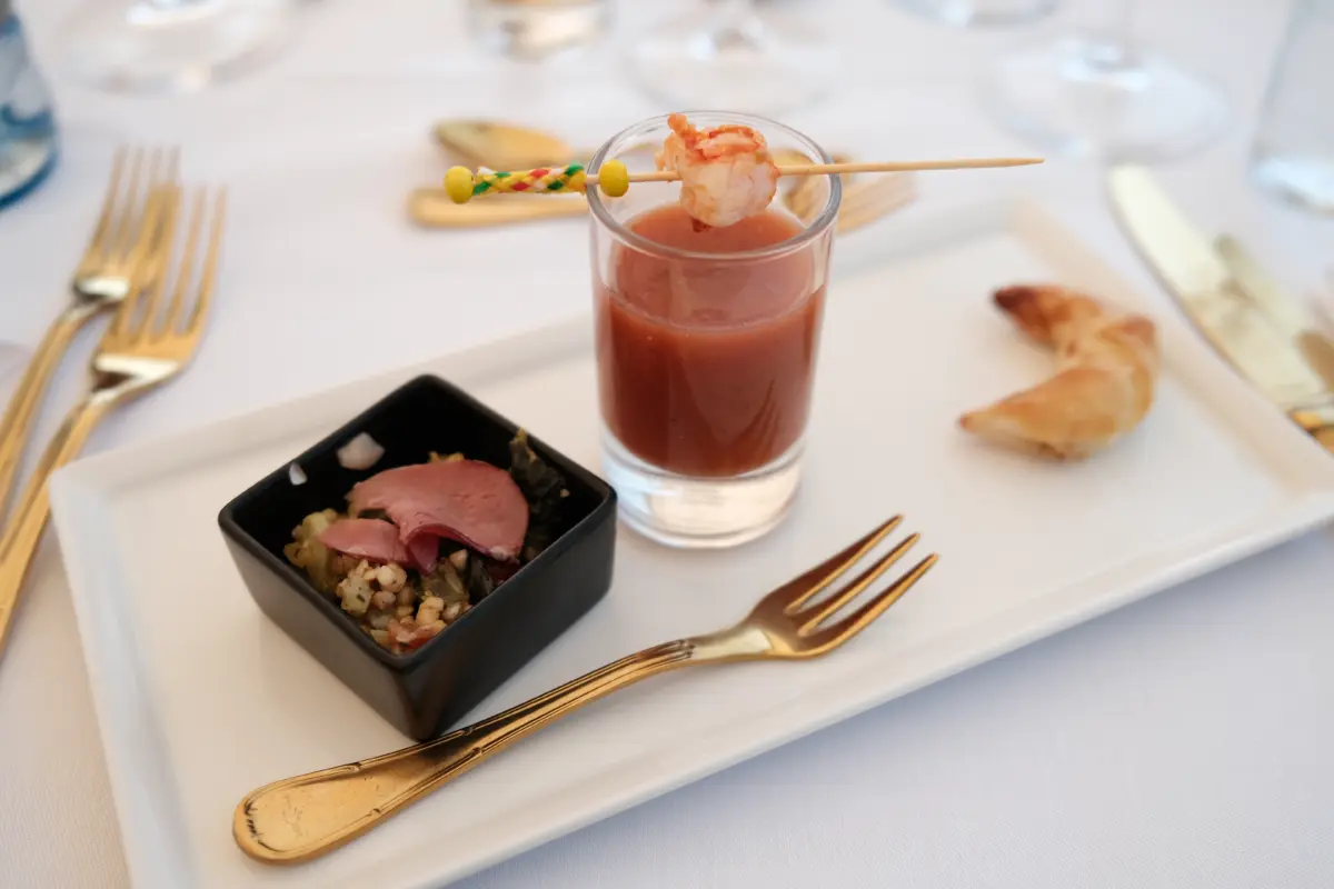 Vorspeise mit Garnelenspieß und Suppe im Glas auf einem gedeckten Tisch an Bord