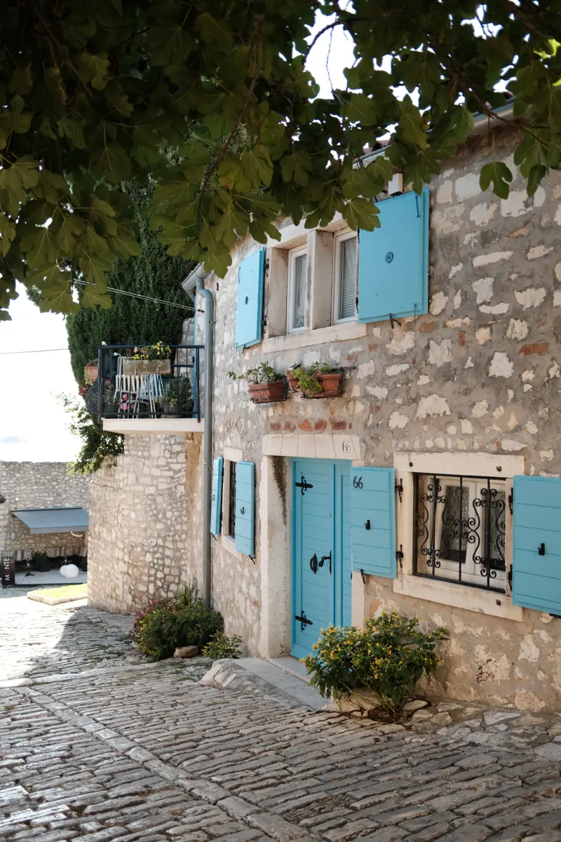 Steinhaus mit hellblauen Fensterläden an einer gepflasterten Gasse
