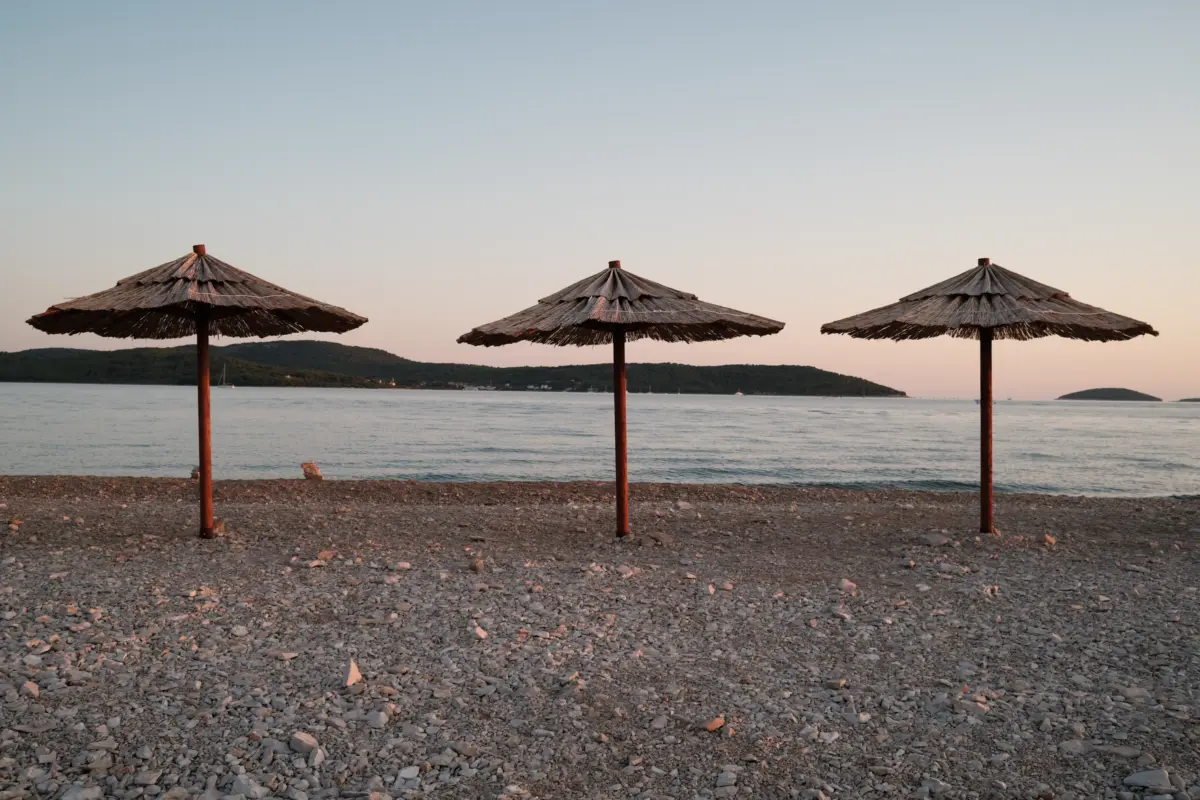Drei Strohschirme am Kiesstrand in der Abenddämmerung