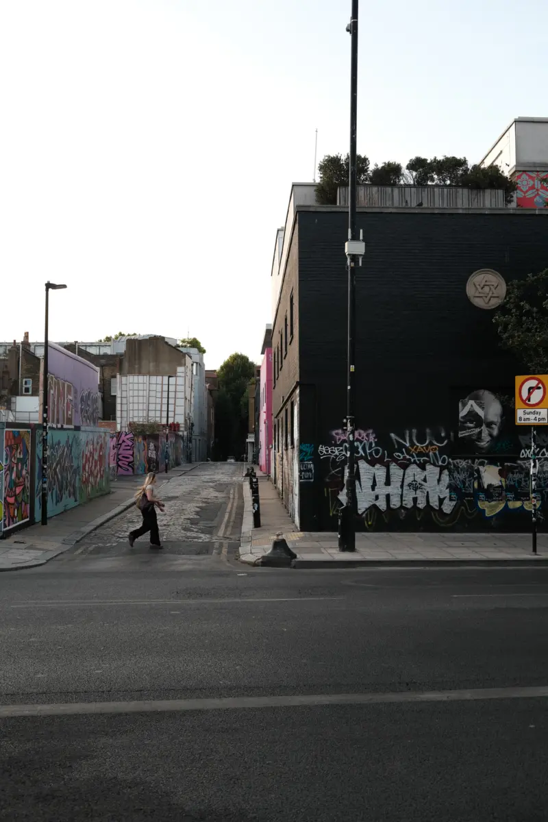 Fußgängerin auf einer Straße zwischen Backsteinbauten mit Graffiti