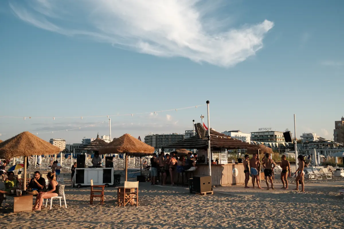Strandbar mit Strohschirmen und Menschen im Abendlicht