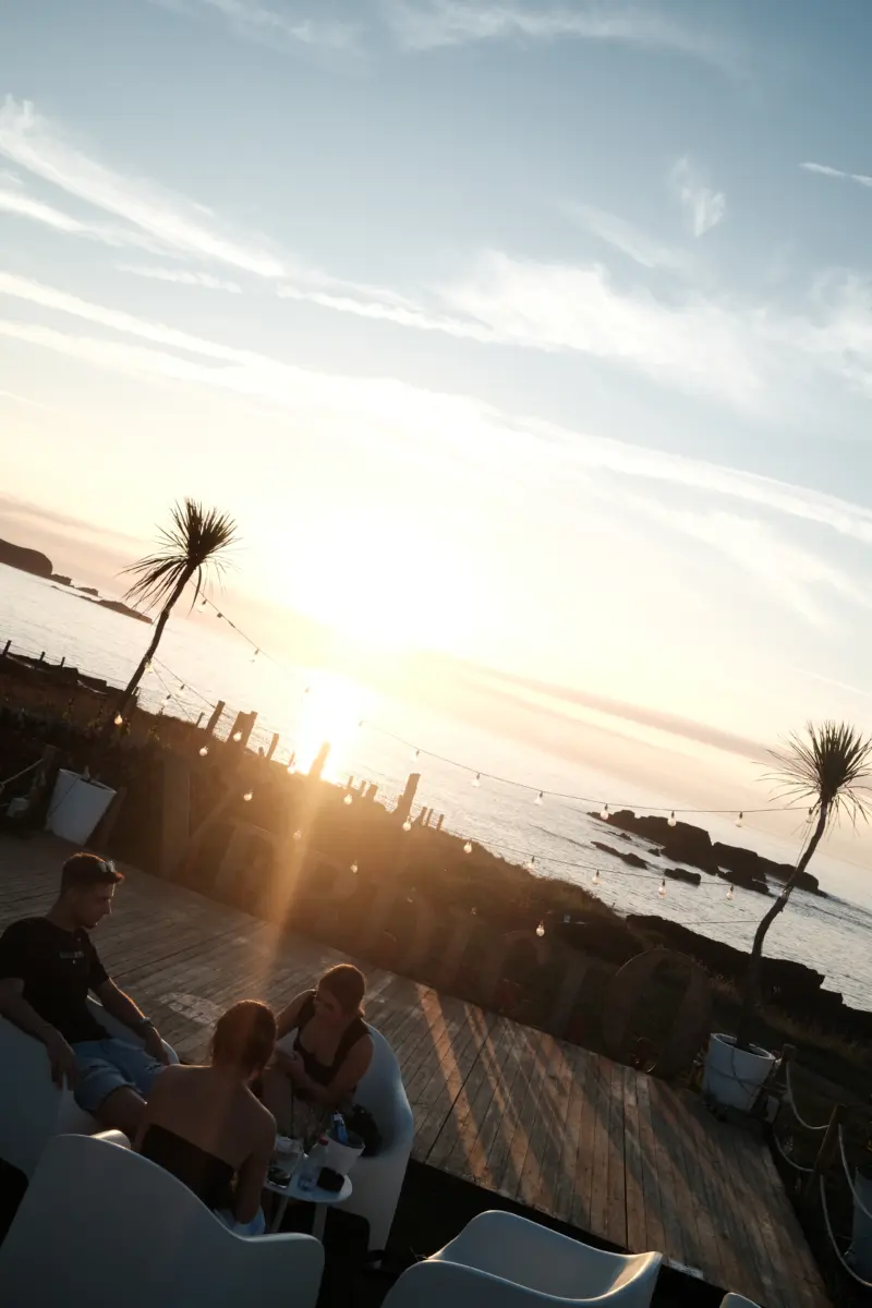 Menschen auf einer Terrasse mit Palmen im Sonnenuntergang