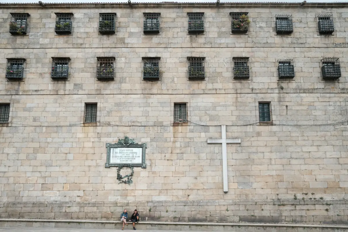 Steinfassade mit vergitterten Fenstern und großem Kreuz