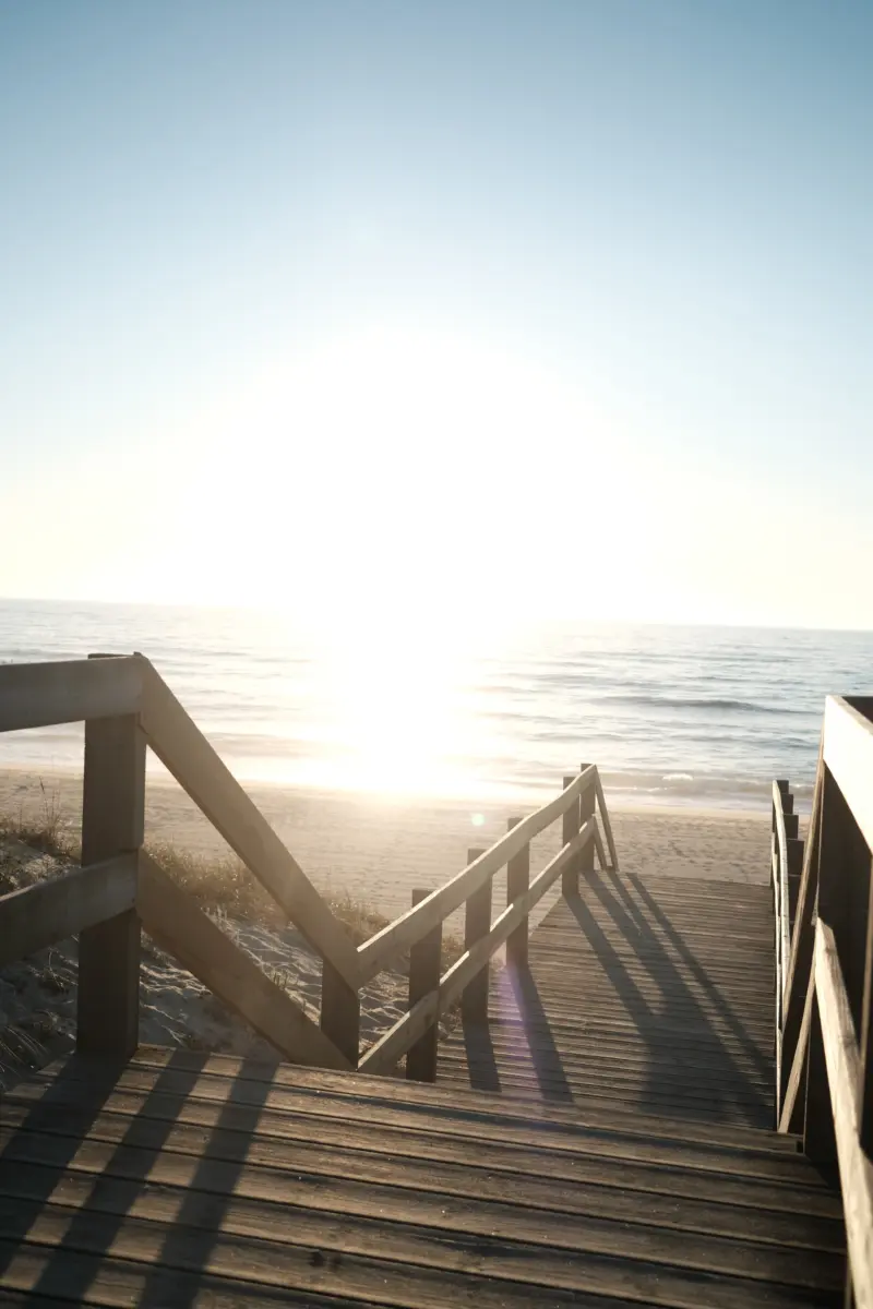 Holzsteg mit Treppe zum Strand im Gegenlicht