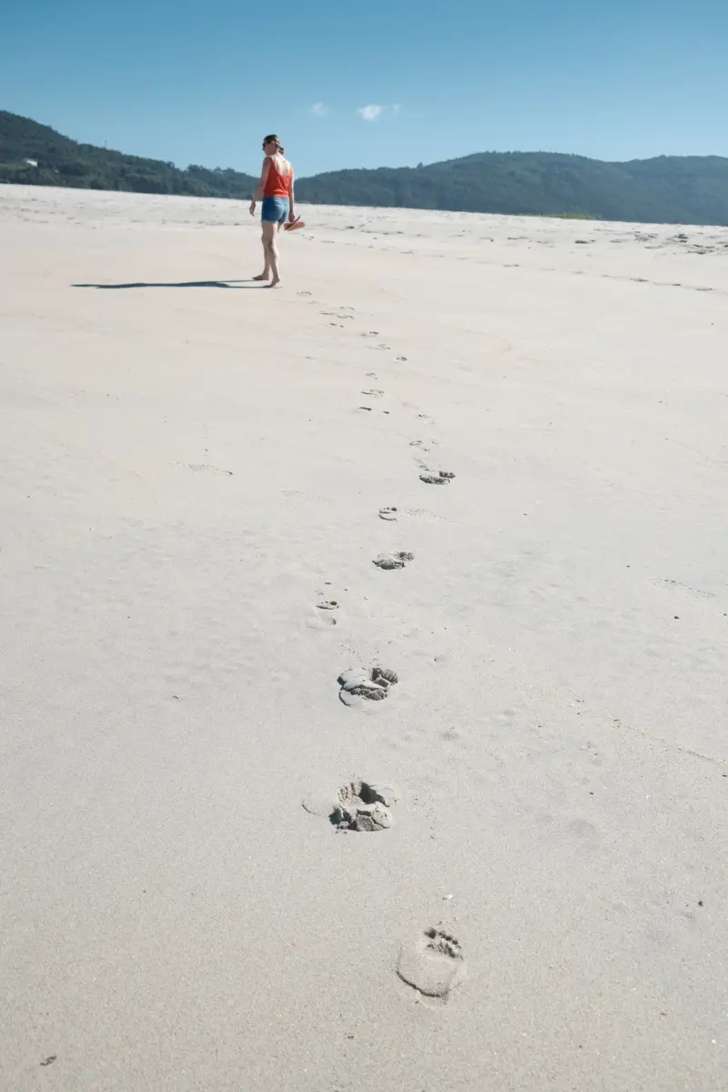 Frau am weiten Sandstrand mit Fußspuren im Sand