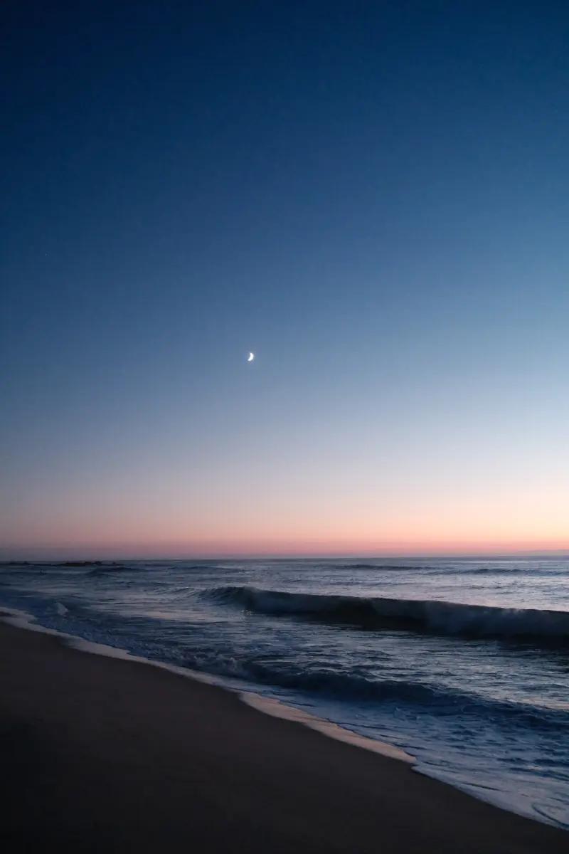 Strand mit Wellen in der Abenddämmerung und Mondsichel