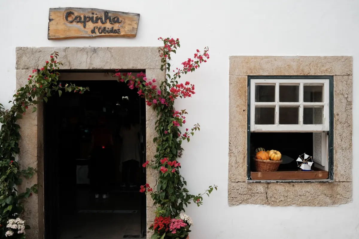 Eingang mit Holzschild „Capinha d’Óbidos“ und blühender Bougainvillea