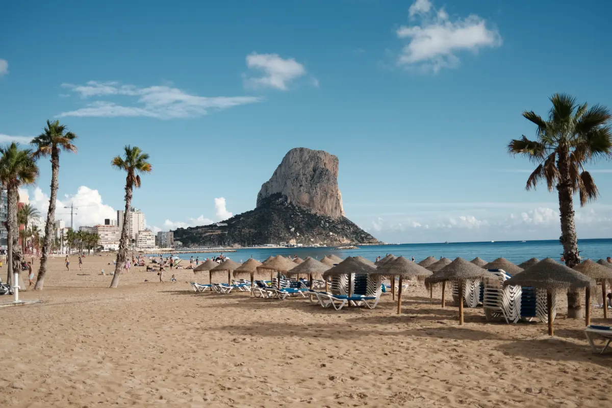 Strand mit Sonnenschirmen und Palmen vor dem Peñón de Ifach