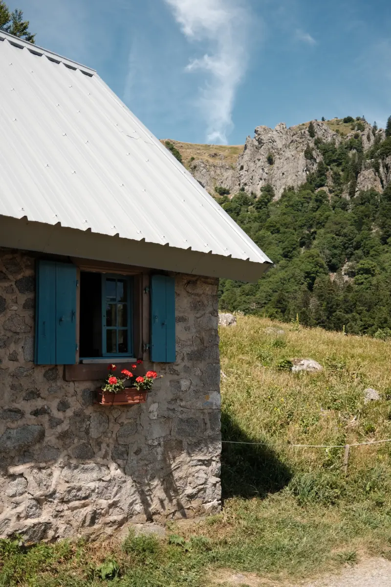 Steinhütte mit blauen Fensterläden und roten Blumen